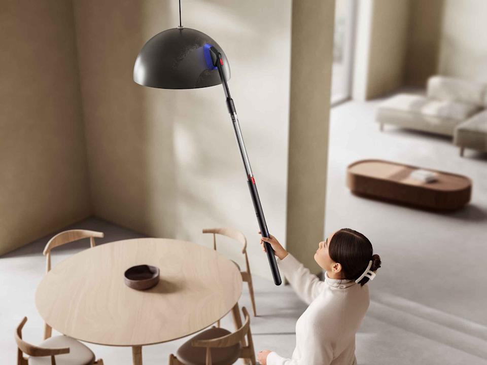 A person using the Dyson PencilVac to clean an overhead light fixture.
