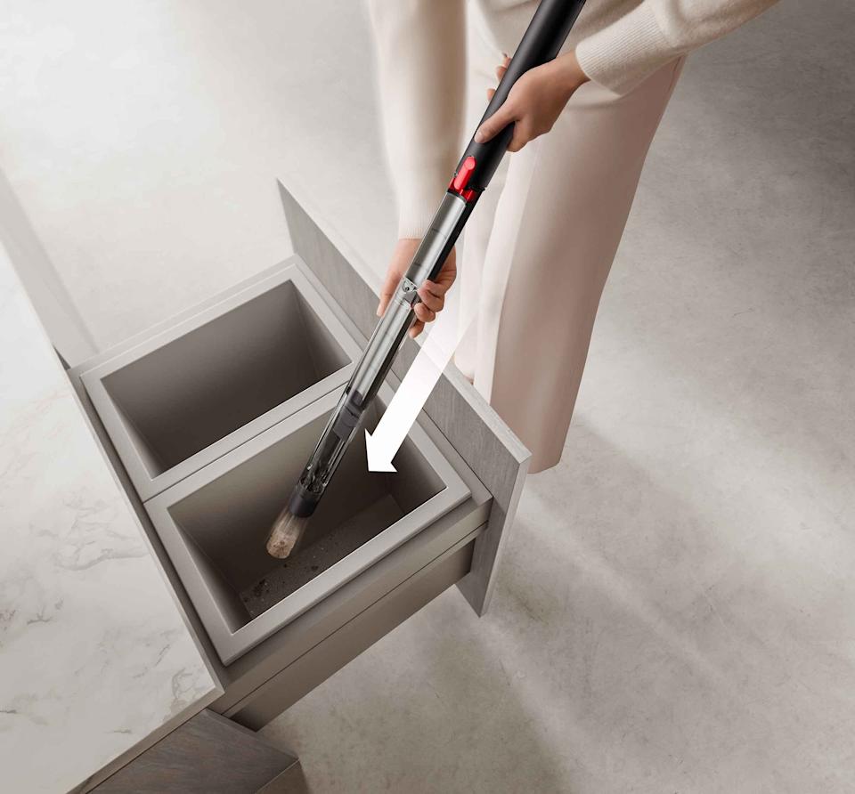 A pair of hands holding the PencilVac over a trash container, with an overlaid arrow indicating downward movement of the vacuum cleaner's bin.