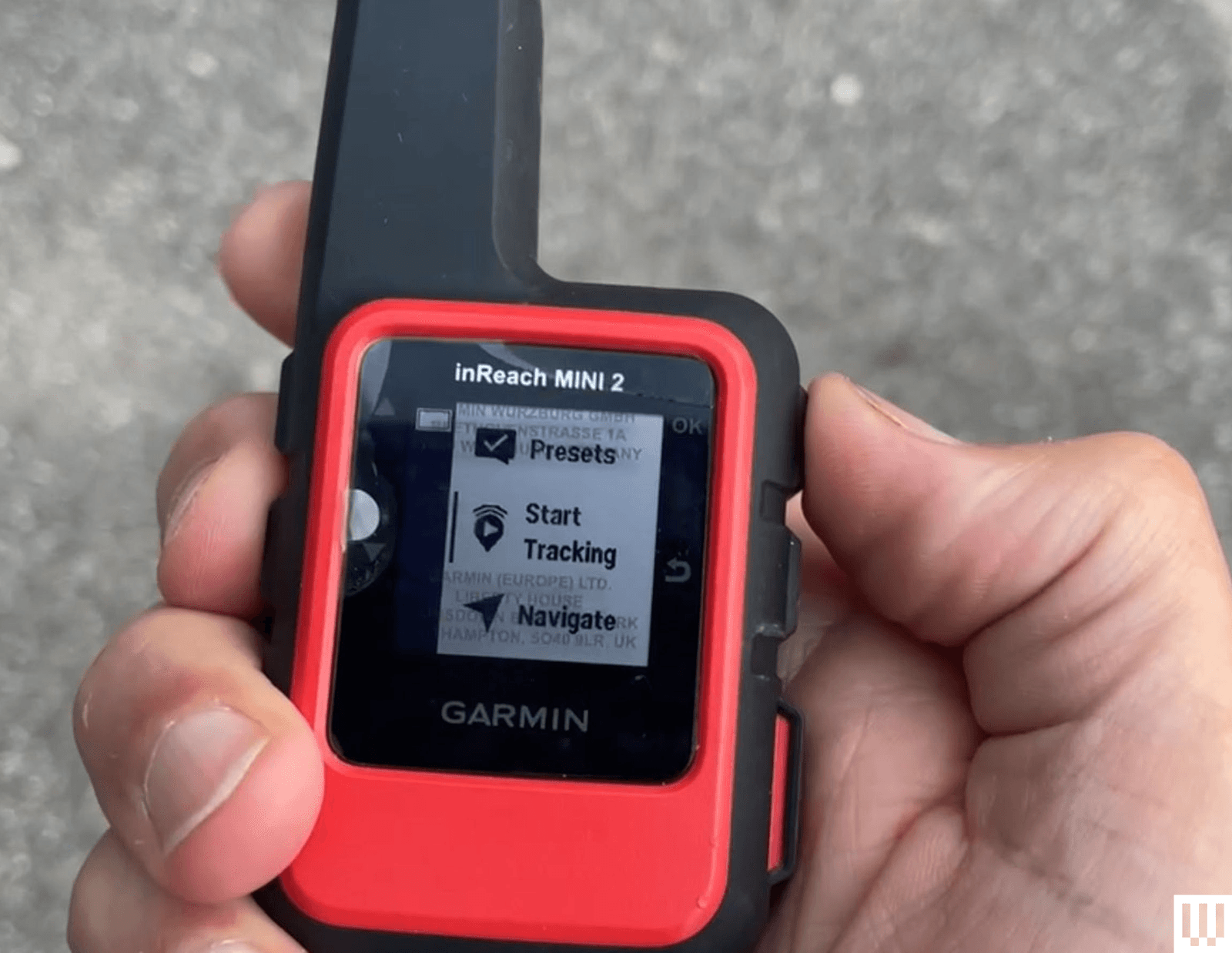 Hand holding small black and red device with a thick antenna and small screen